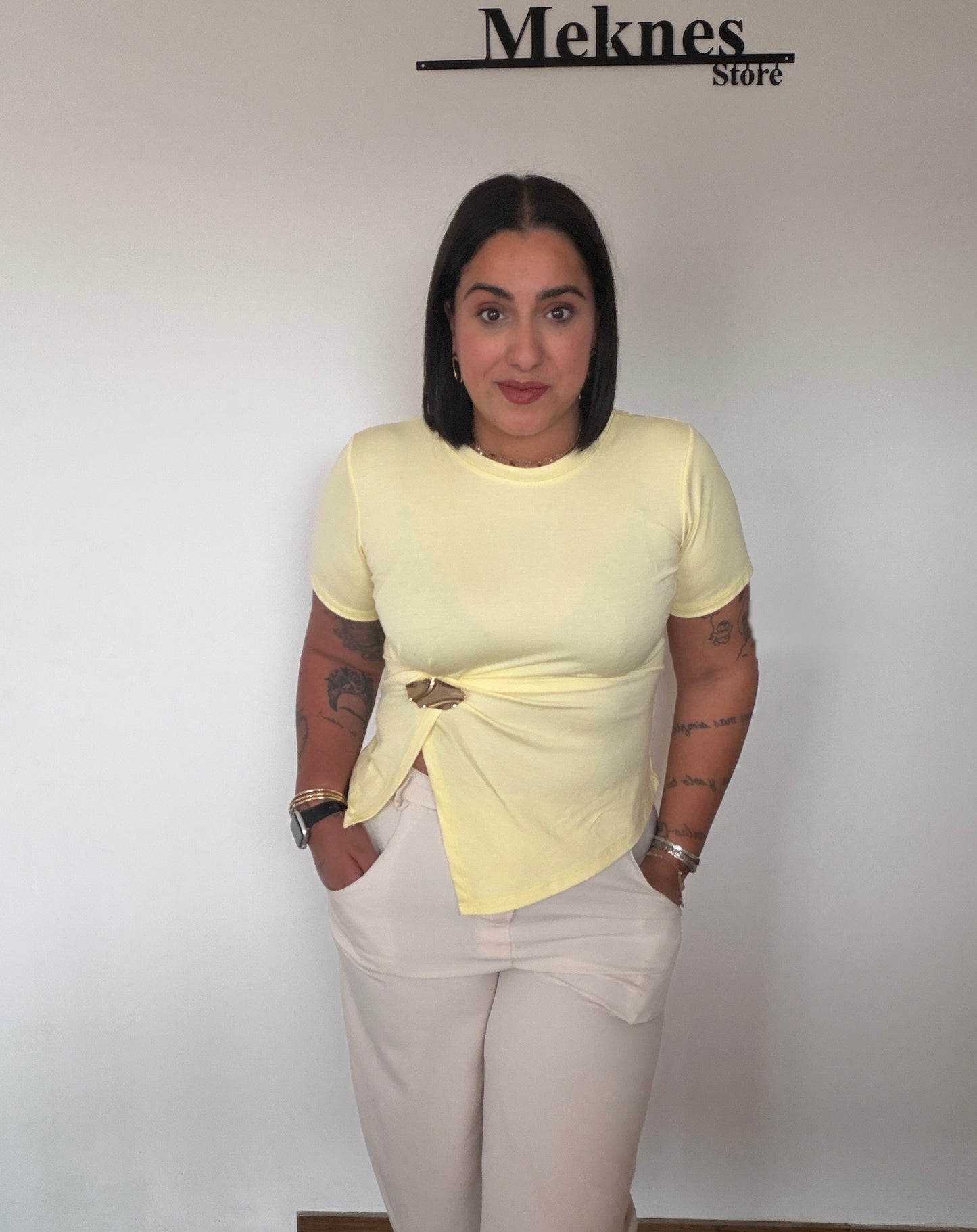 Modelo luciendo camiseta amarilla asimétrica con broche joya dorado