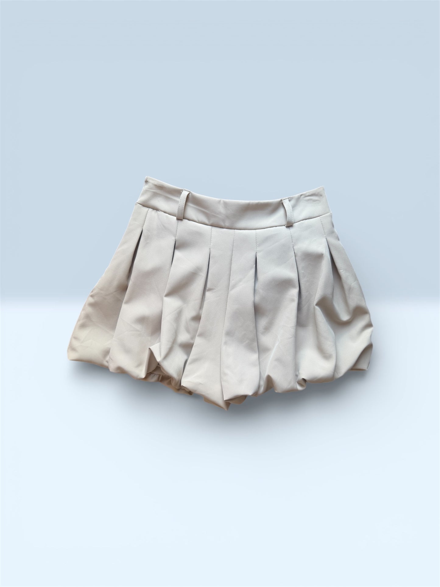 Detalle falda beige corta con vuelo y pliegues estilo bubble.
