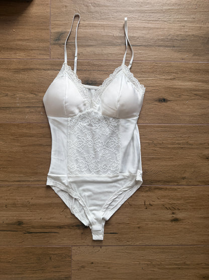 Body blanco de raso y encaje sobre suelo madera, detalle tejido suave.