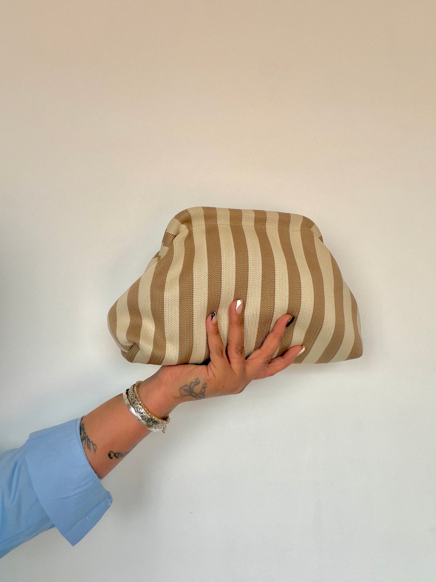 olso de mano estilo clutch con rayas verticales en tonos beige y blanco mostrado en la mano Meknes Store