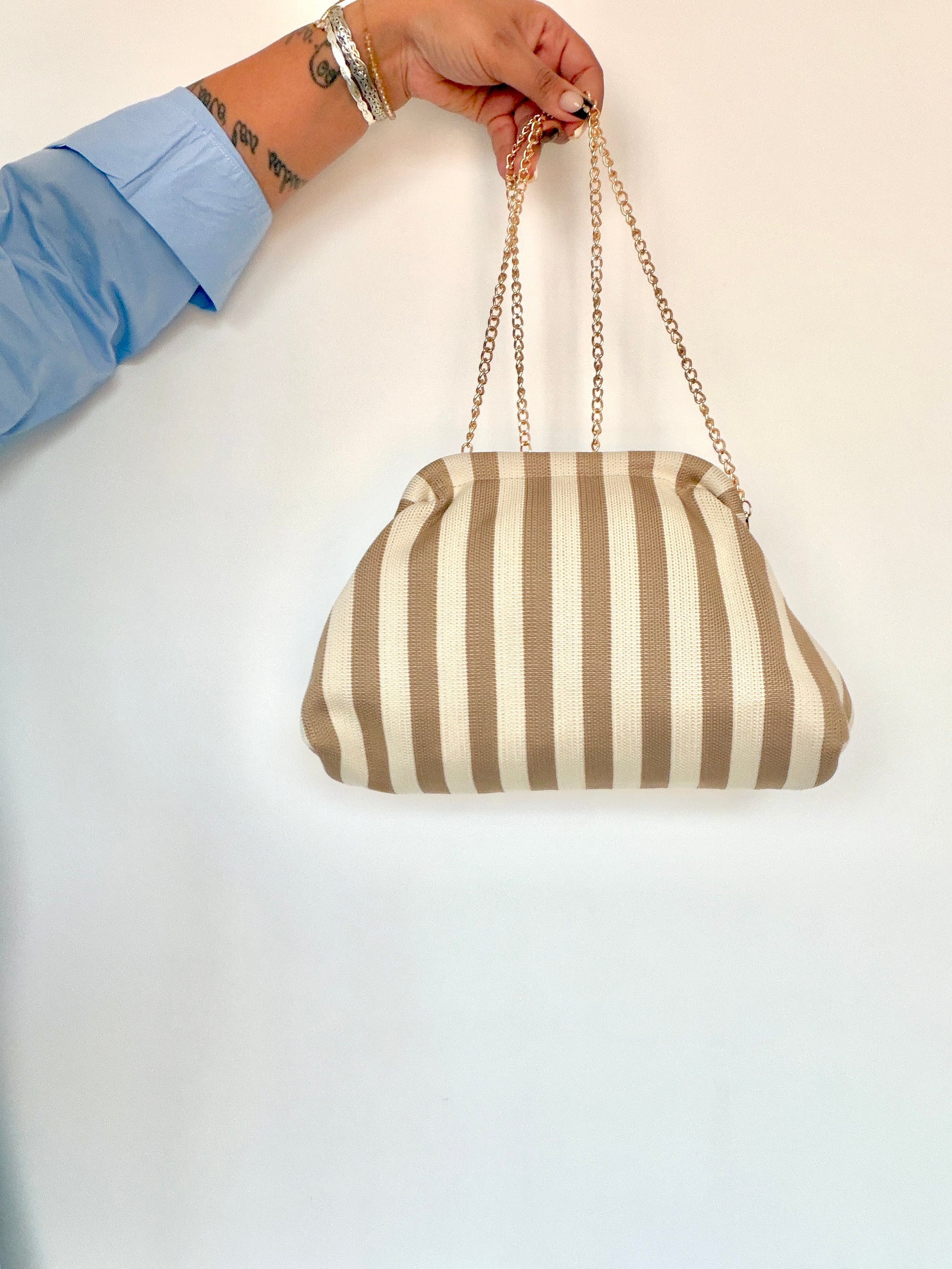 Bolso de mano Stripes colgado de su cadena dorada sobre fondo blanco Meknes