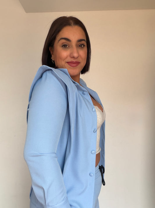 Detalle chaqueta fluida azul cielo abierta con crop top blanco y pantalón a juego.