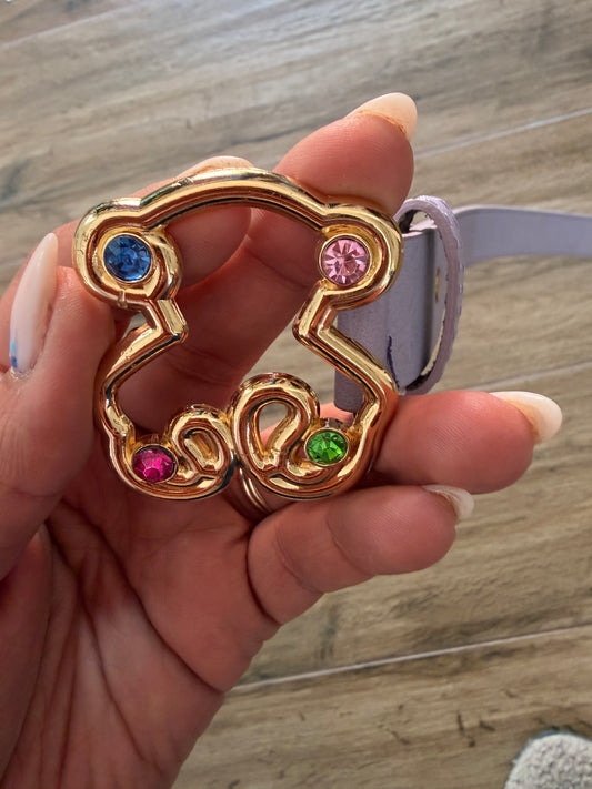 Primer plano de hebilla metálica dorada de oso con cristales de colores en cinturón malva