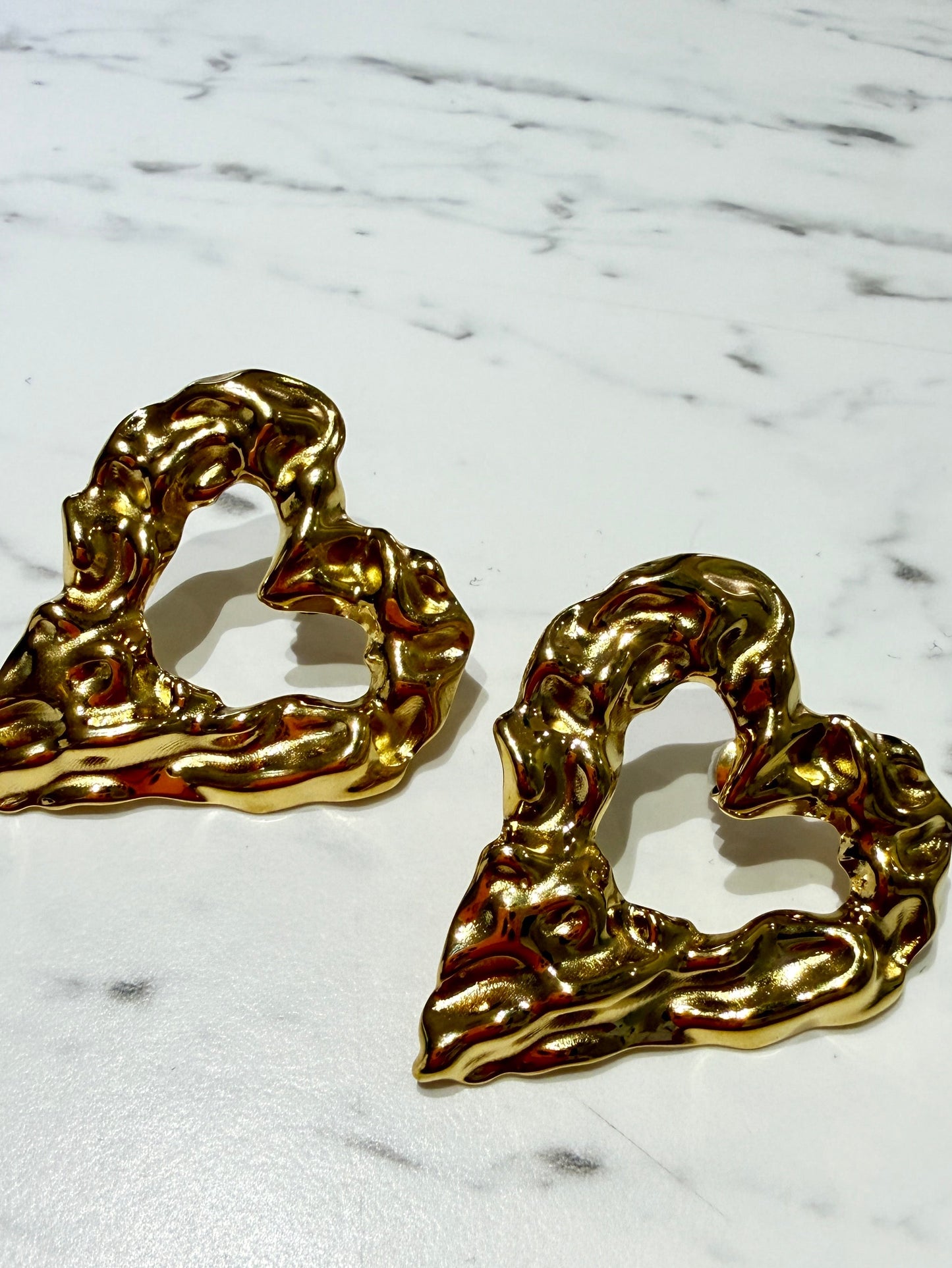 Primer plano de pendientes dorados con textura irregular de metal fundido sobre mármol