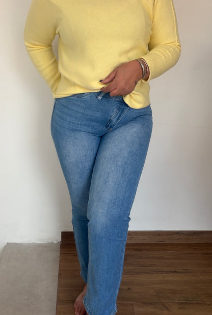 Mujer con vaqueros de cintura asimétrica cruzada y jersey amarillo.