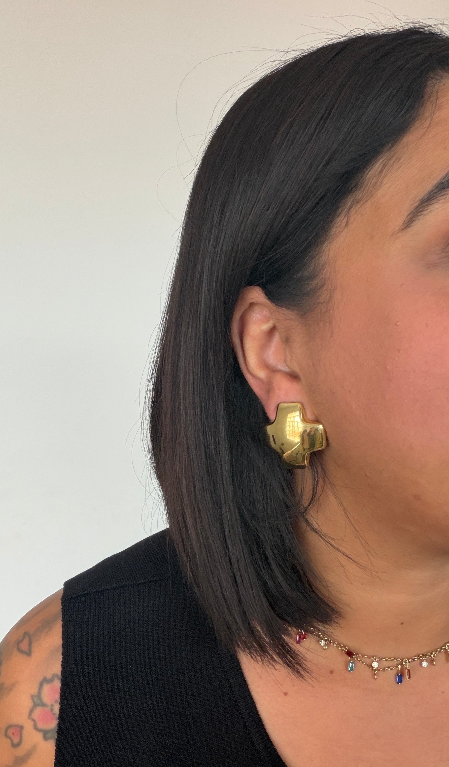 Perfil de mujer luciendo pendientes dorados brillantes con diseño de cruz moderna