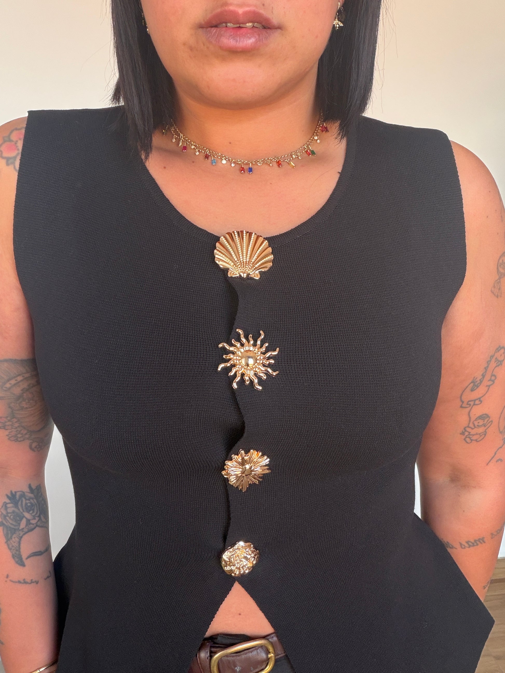 Primer plano top negro mostrando botones dorados de soles y conchas marinas